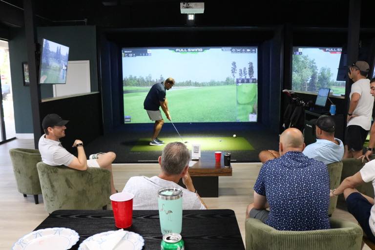 Friends in the lounge watching a golfer tee off on a Full Swing simulator
