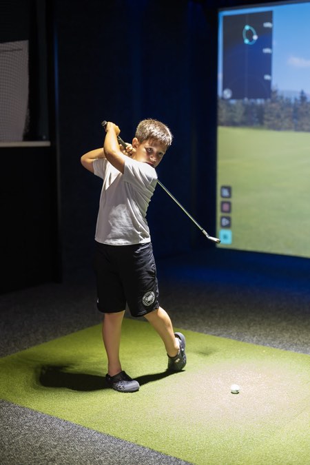 A young golfer finishing his swing on a Full Swing simulator