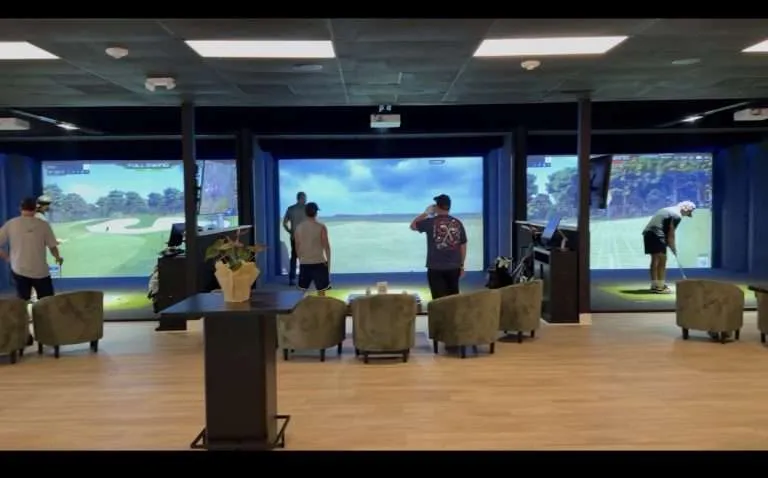 Golfer swinging on a simulator while friends watch from the lounge