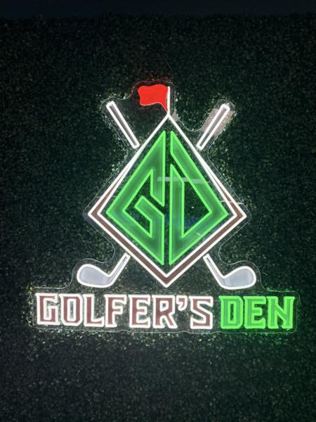 Golfer's Den neon sign on a green hedge wall